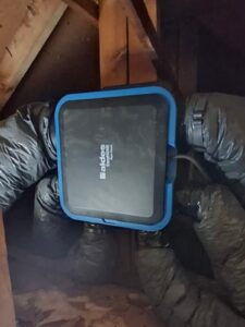 Caisson VMC hygroréglable Aldes extra-plat fixé sur la charpente, avec quatre raccordements sanitaires et une extraction cuisine.