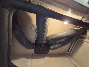 Caisson VMC hygroréglable Atlantic Hygrocosy fixé au plafond en pièce technique avec raccordement des gaines de ventilation.